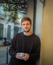 Alexander Hecking, founder coach, leaning on a wall with a coffee cup
