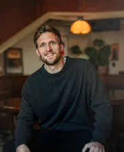 Alexander Hecking, founder coach, seated indoors in warm café light