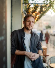 Alexander Hecking, founder coach, on a street with a café terrace behind him